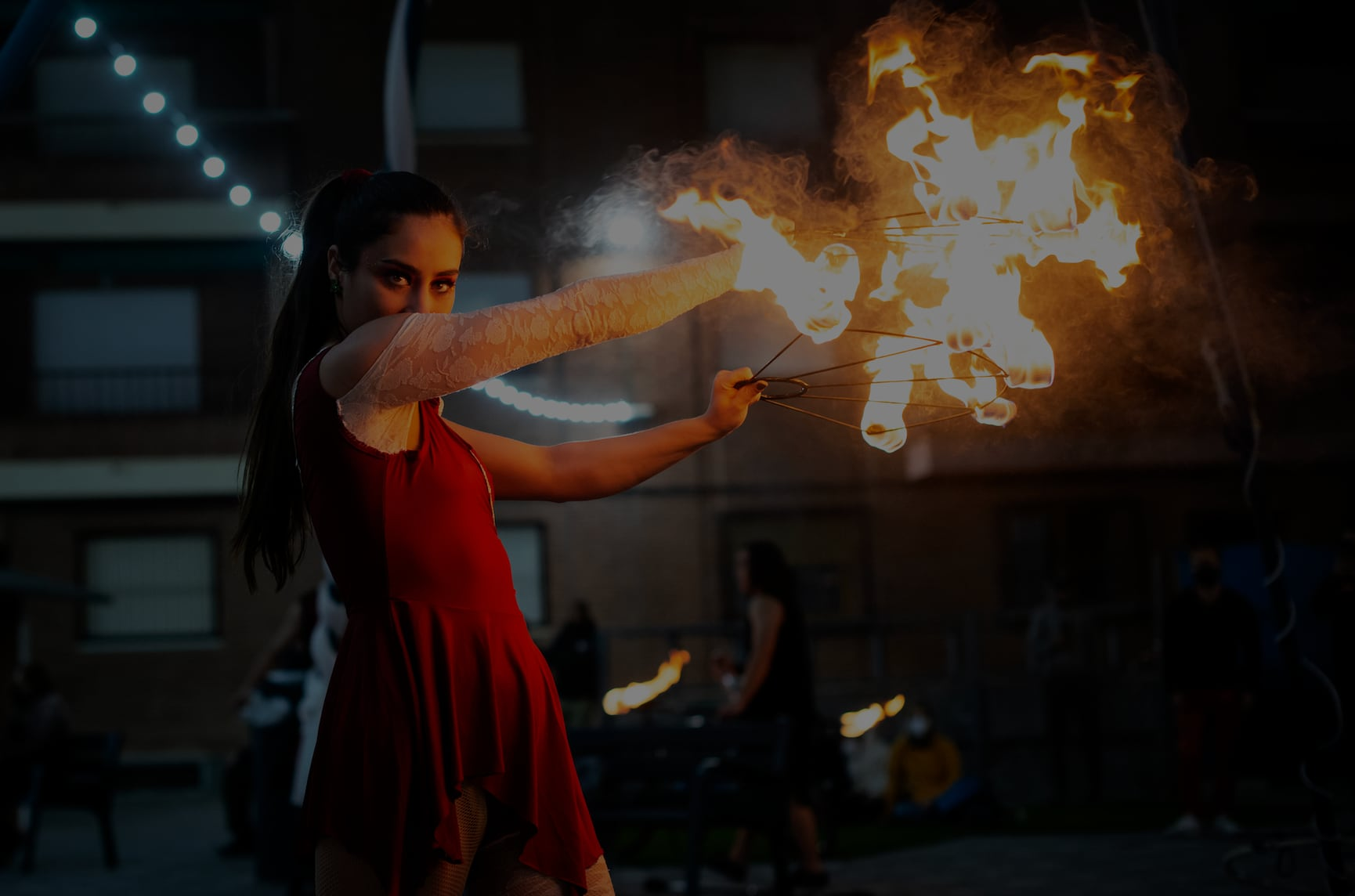 Performer in a red dress juggling fire fans during a night-time performance