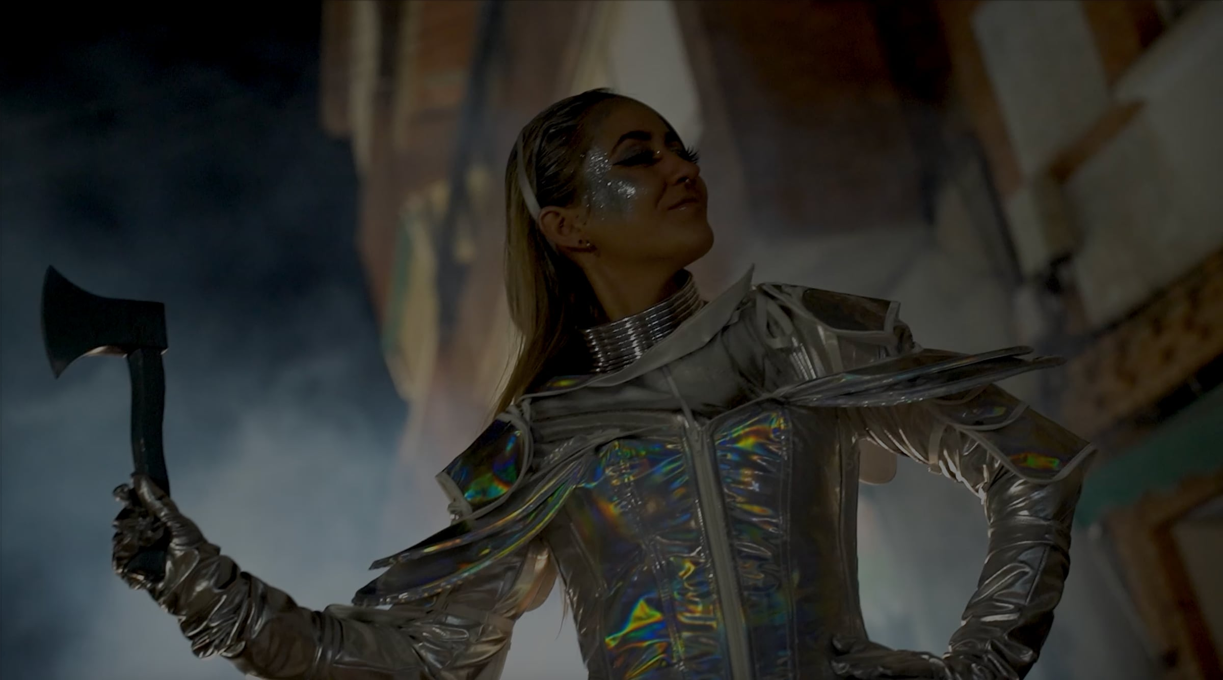 Performer dressed as the Tin Man in an iridescent silver costume holding an axe, surrounded by stage smoke